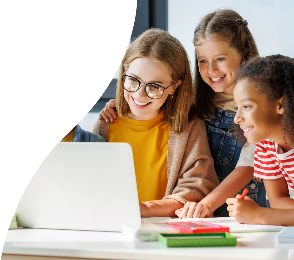 Eine Frau mit Pagenschnitt und Brille blickt lächelnd auf den Bildschirm eines Laptops. Um Sie herum sind Jungen und Mädchen von etwa sechs, sieben Jahren, die interessiert und fröhlich auf den Monitor schauen.