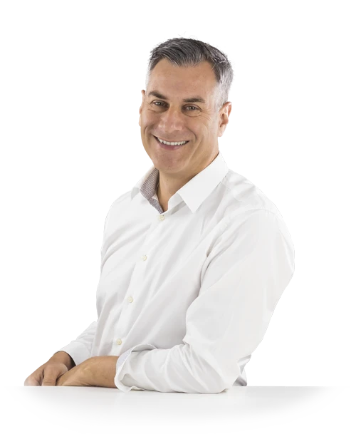 Jochen Muffler stands leaning against a table in a white shirt and looks into the camera with a smile.